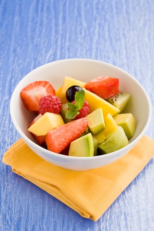 photo of colorful fruit salad on blue glass table with small mint leafの写真素材