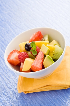 photo of colorful fruit salad on blue glass table with small mint leafの写真素材