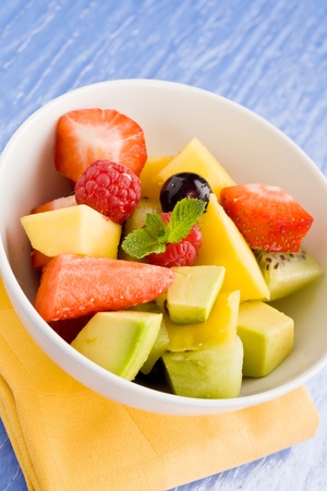 photo of colorful fruit salad on blue glass table with small mint leafの写真素材