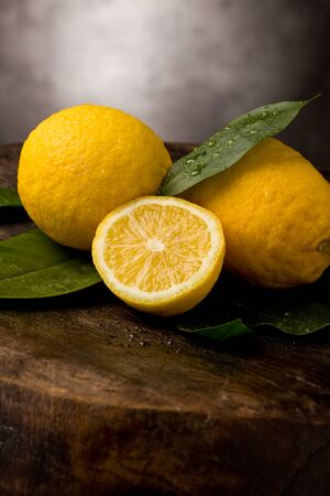 photo of fresh yellow lemons with leaves and water drops on wooden tableの写真素材