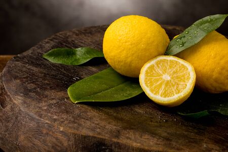 photo of fresh yellow lemons with leaves and water drops on wooden tableの写真素材