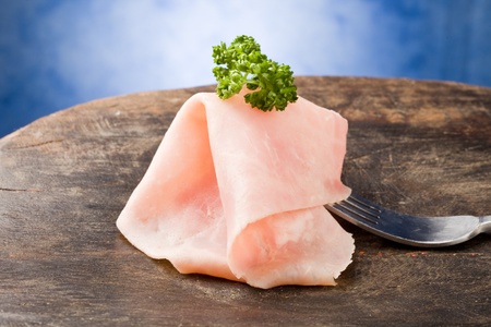 photo of sliced ham holded by fork with parsley on it の写真素材
