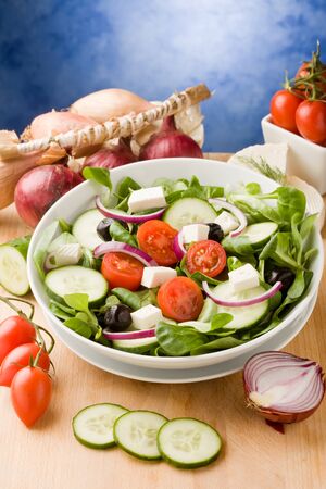 photo of delicious greek salad on wooden table in front of blue background with spot lightの写真素材