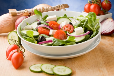 photo of delicious greek salad on wooden table in front of blue background with spot lightの写真素材