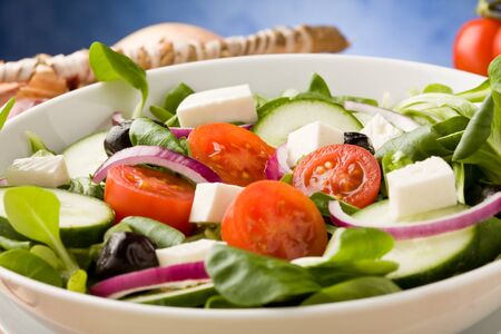 photo of delicious greek salad on wooden table in front of blue background with spot lightの写真素材