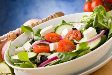 photo of delicious greek salad on wooden table in front of blue background with spot lightの写真素材