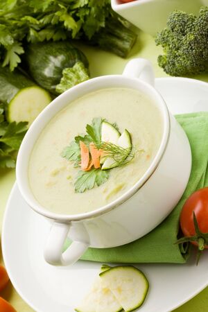 photo of vegetarian vegetable soup on green wooden table with different vegetables arroundの写真素材