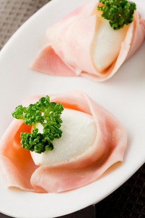 photo of delicious mozzarella with wrapped ham on wooden tableの写真素材