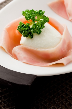 photo of delicious mozzarella with wrapped ham on wooden tableの写真素材