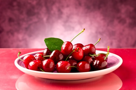 photo of delicious fresh cherries inside a plate on red reflecting tableの写真素材