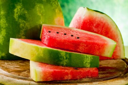 photo of fresh delicious watermelon on chopping board with green backgroundの写真素材