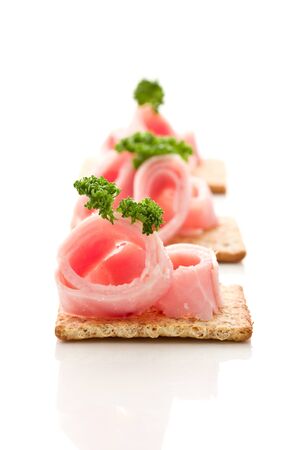 photo of delicious crackers with ham and parsley on white backgroundの写真素材