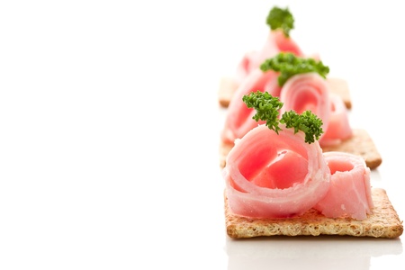 photo of delicious crackers with ham and parsley on white backgroundの写真素材