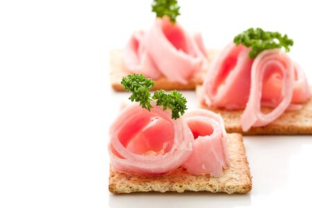 photo of delicious crackers with ham and parsley on white backgroundの写真素材