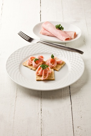 photo of cracker appetizer with  ham and parsley on white wooden tableの写真素材