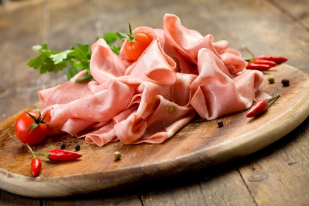 wooden chopping board with sliced mortadella and red pepperの写真素材