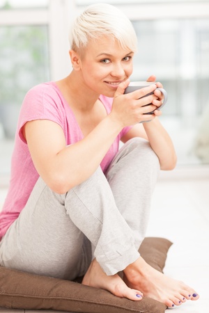 Photo of smiling woman with mug sitting on the floor while smilingの写真素材