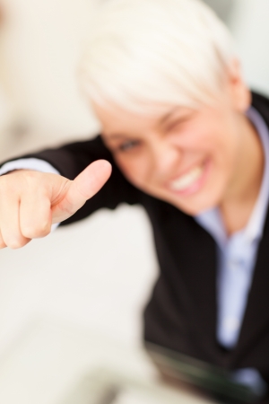 Businesswoman making positive thumb gesture while smiling in the officeの写真素材