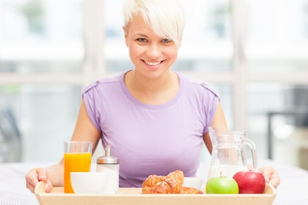 Young blonde woman is having breakfast in the bedroomの写真素材