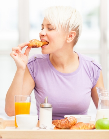 Young blonde woman is having breakfast in the bedroomの写真素材
