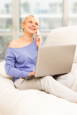 Photo of smiling woman on the sofa with computer and phoningの写真素材