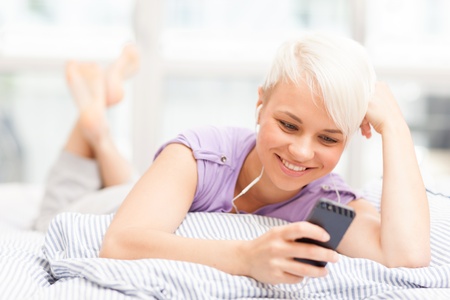 young woman phoning in the bed with headphonesの写真素材