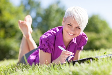 Beautiful female student is studying in a green fieldの写真素材