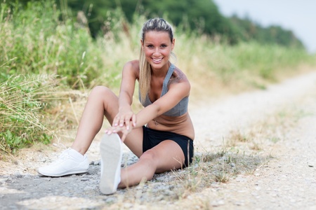 Photo of smiling blonde woman doing stretching exercises on a field streetの写真素材