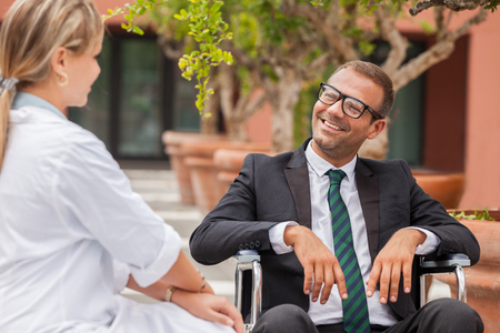 Smiling businessman on wheelchair looking towards his doctorの写真素材