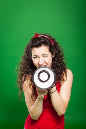 Photo of young woman screaming through megaphone over green backgroundの写真素材