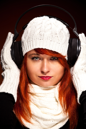 Photo of red hair woman with winter outfit listens to music with headphonesの写真素材