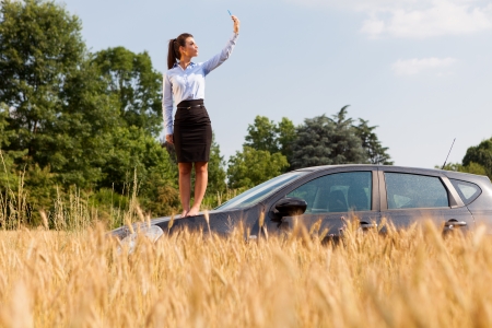 Brunette businesswoman searching for phone signal while standing on her carの写真素材