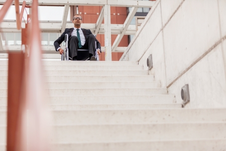Conceptual photo of businessman on wheelchair in front of stairsの写真素材