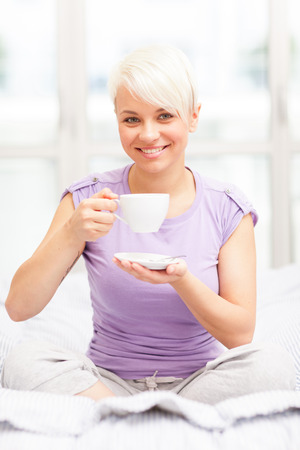 Photo of lovely blonde woman drinking coffee in her bedの写真素材