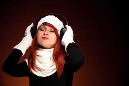 Photo of red hair woman with winter outfit listens to music with headphonesの写真素材