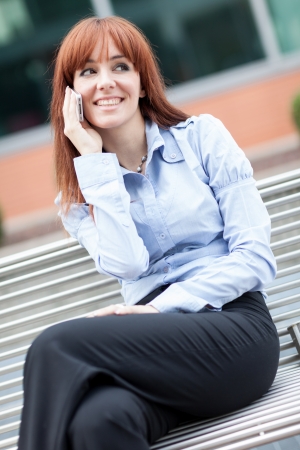 Business photo of red hair businesswoman sitting on a metal bench while phoningの写真素材