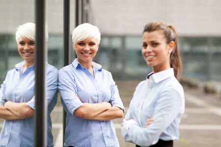 Two smiling and successful businesswoman next to a glass wallの写真素材