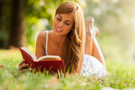 Photo of woman laying in a grass field while reading a bookの写真素材