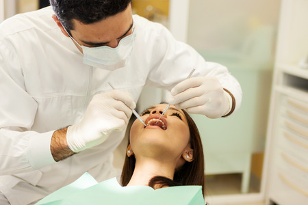 photo of caucasian male dentist visiting his young asian female patient in a dentist officeの写真素材