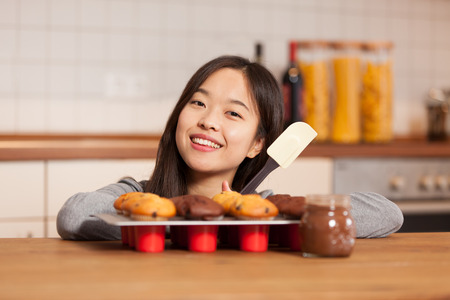 photo of smiling asian woman in the kitchen with tray full of muffinsの写真素材