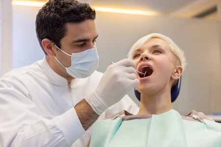 caucasian dentist looking inside the mouth of his young blonde patientの写真素材