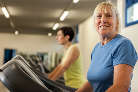 Portrait of caucasian mature woman looking towards the camera while running on a treadmill in the fitness studioの写真素材