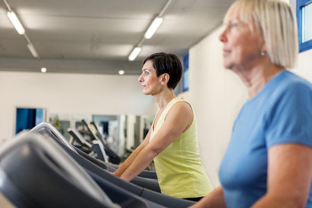 Two mature women are running on a treadmill in the fitness studio