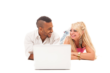 Smiling couple lying on the floor with notebook over white isolated backgroundの写真素材