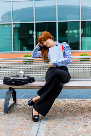 Photo of businesswoman with red hair sitting outside on a metal bench while smilingの写真素材