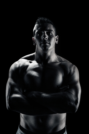 Low light portrait of bodybuilder with crossed hands over black backgroundの写真素材
