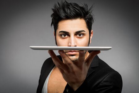 Closeup of man holding tablet pc on one hand in front of his face over grey backgroundの写真素材