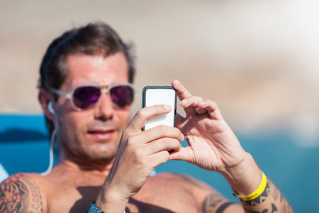 Caucasian man is checking his phone while relaxed on the beachの写真素材