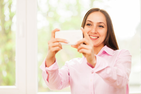 Smiling caucasian woman with pink shirt is doing a selfie with her phoneの写真素材