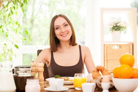 Portrait of smiling young woman having breakfast at homeの写真素材